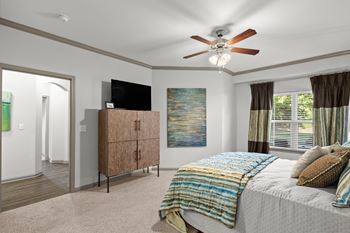 A bedroom with a ceiling fan, large windows, carpeting, and crown molding.